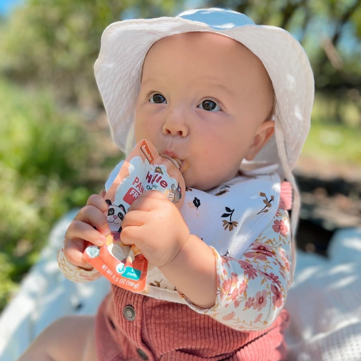 Baby wearing a white hat and pink outfit, enjoying panda peach pouch