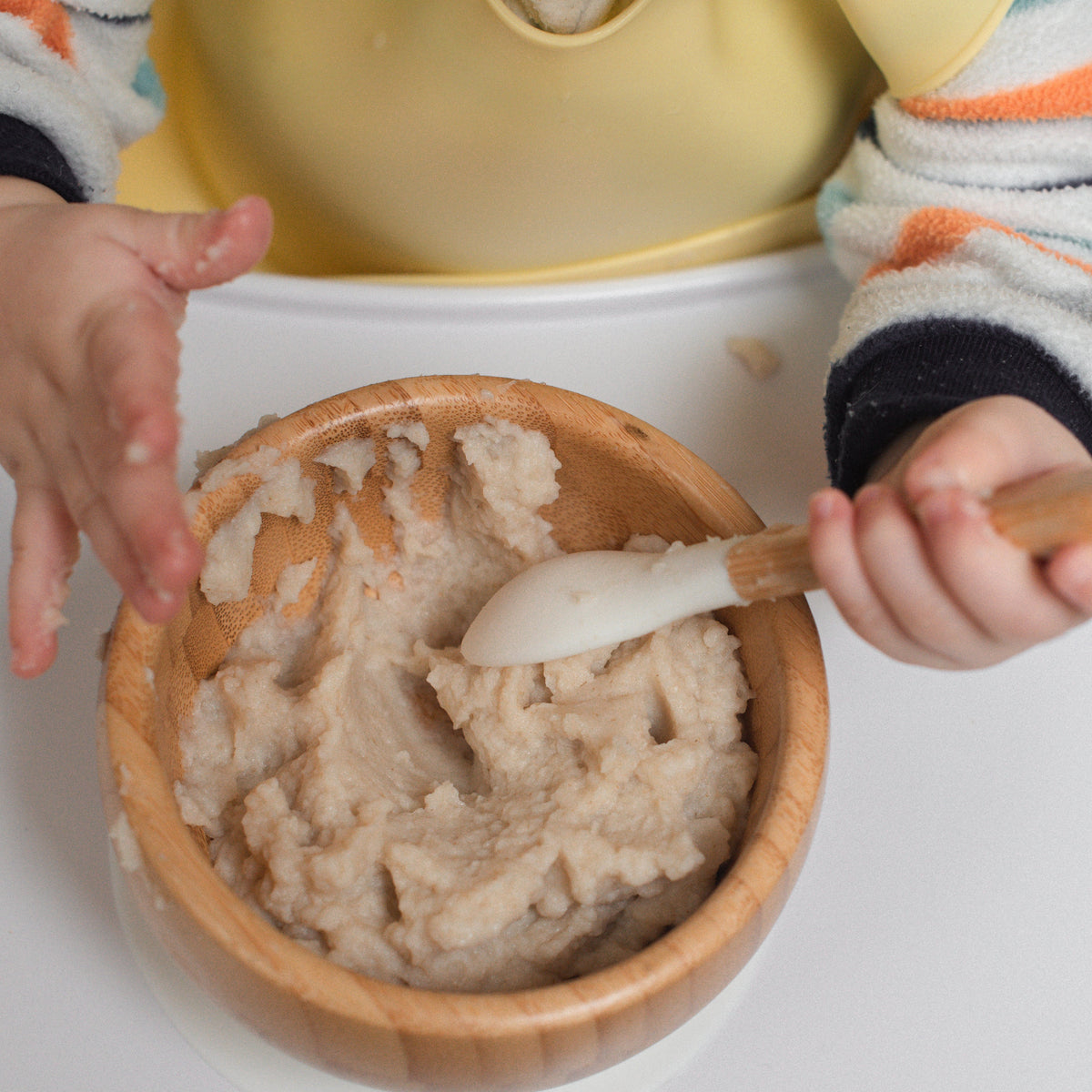baby in a high chair eating cereal. zoomed in on hands holding spoon