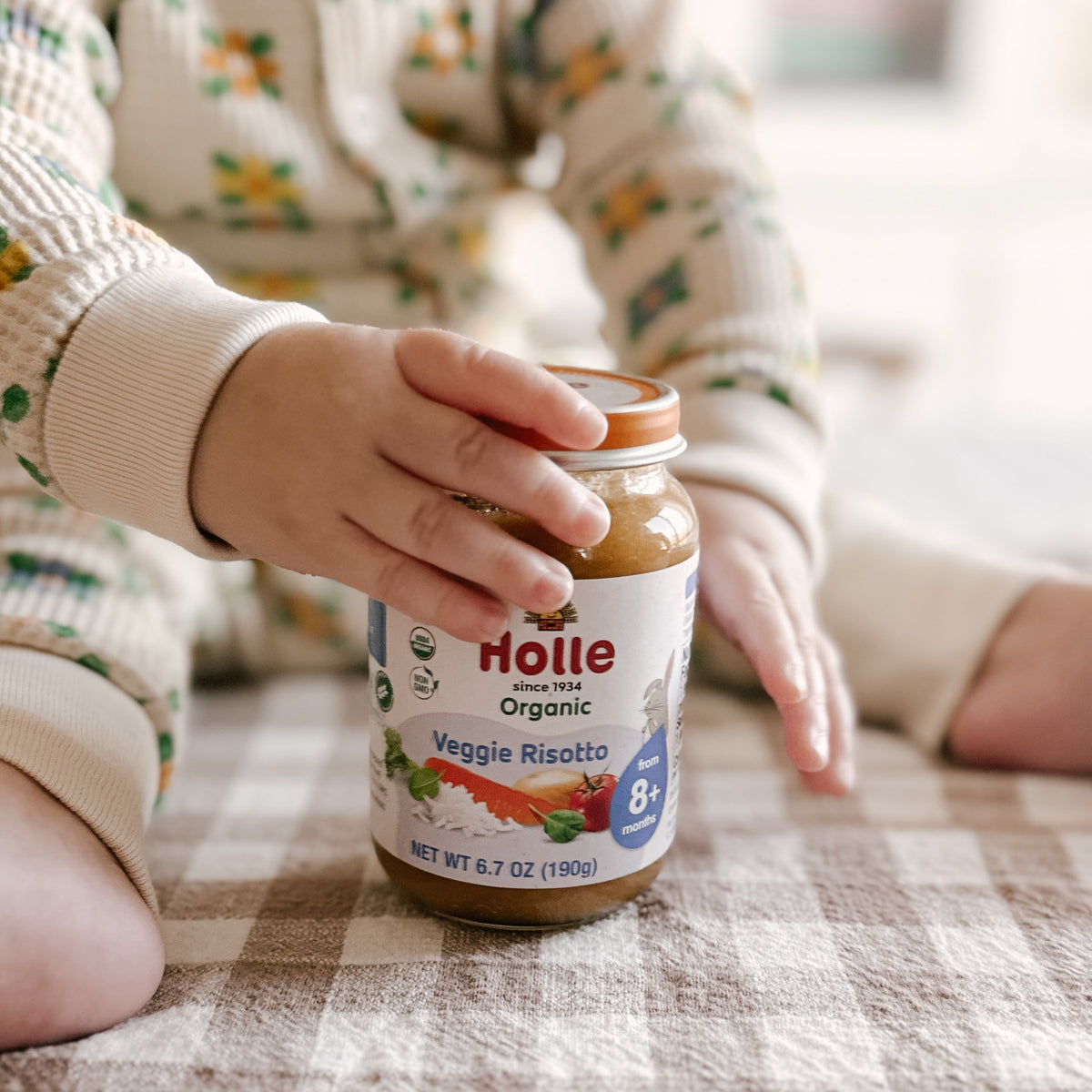 baby hands holding Holle Veggie Risotto baby food jar