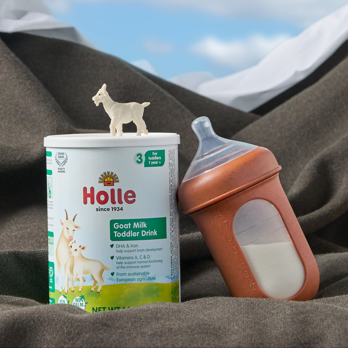 goat milk toddler drink with made bottle and toy goat in mountain of blankets