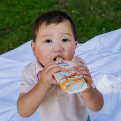 baby enjoying banana llama fruit pouch at a picnic outside