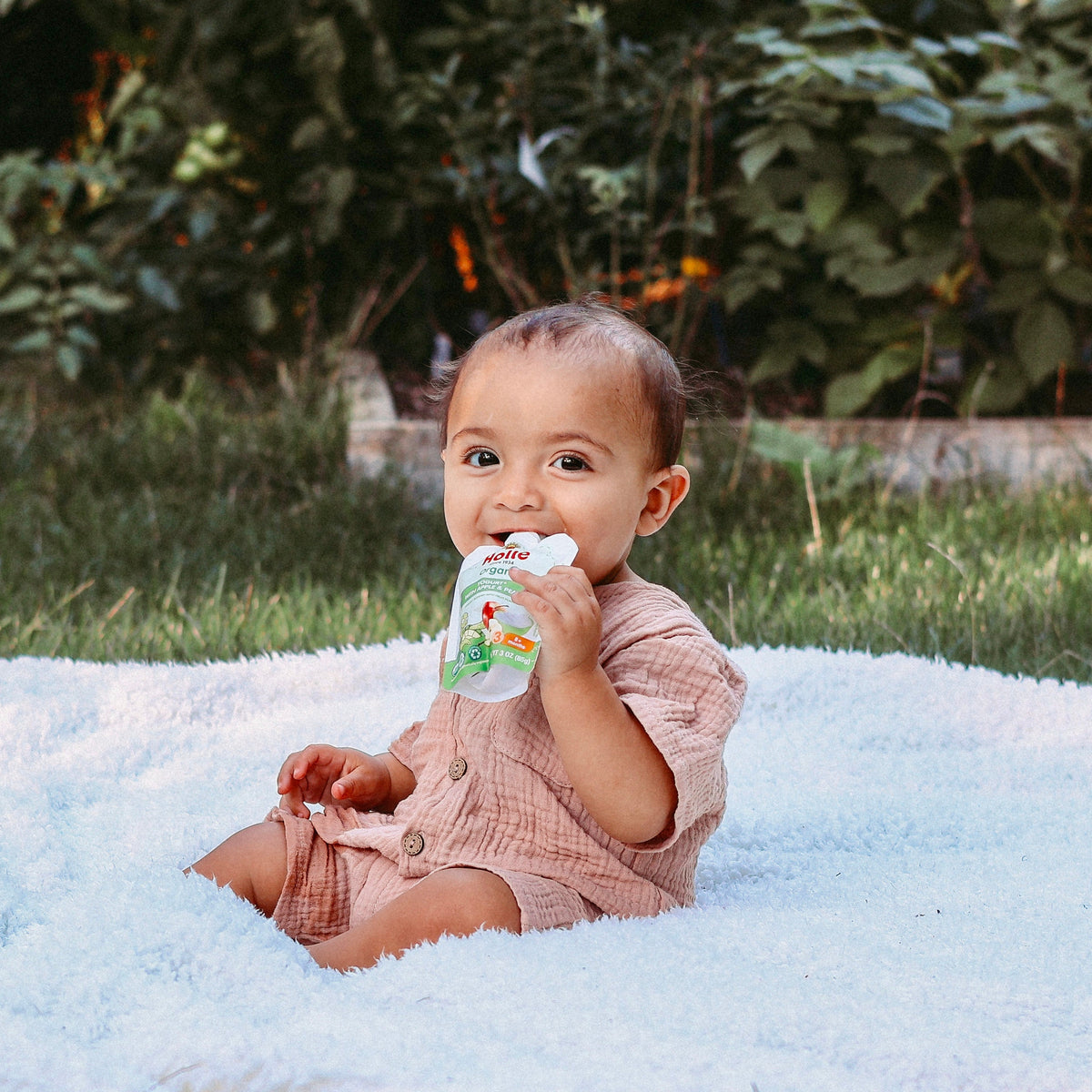 toddler enjoying apple pear yogurt pouch outside on a blanket