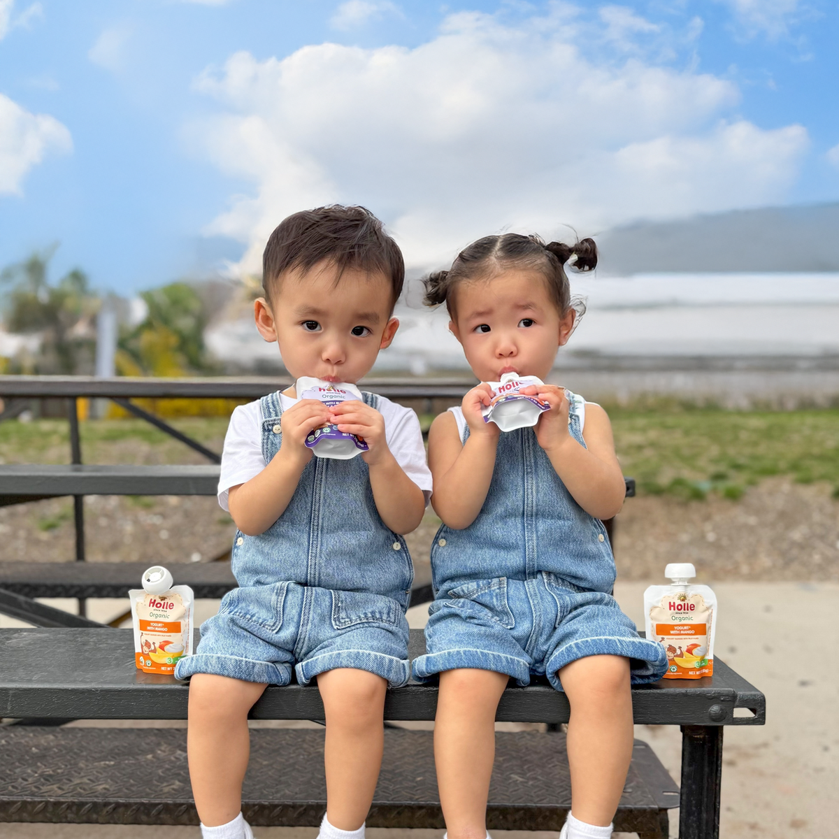 two young kids enjoying toddler yogurt pouches outside on a picnic table
